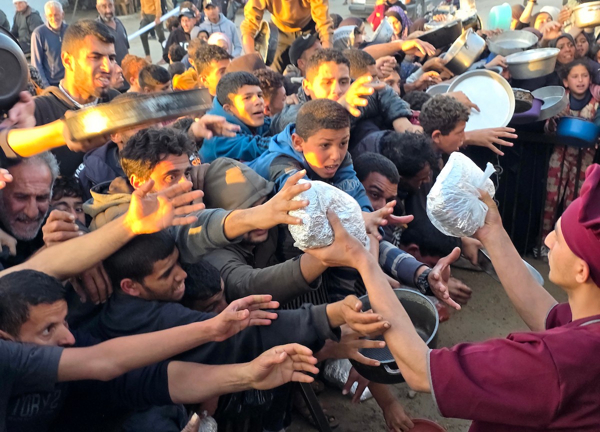 فلسطينيون نازحون يكافحون للحصول على طعام مُتبرع به للإفطار، وجبة كسر الصيام، في اليوم الرابع من شهر رمضان المبارك في مطبخ مجتمعي في خان يونس، قطاع غزة، 21 فبراير/شباط 2026. تصوير: طارق محمد/(APA Images)