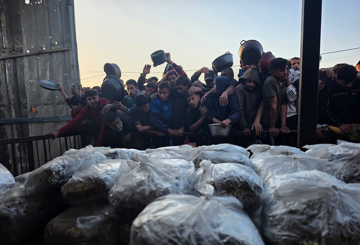 فلسطينيون نازحون يكافحون للحصول على طعام مُتبرع به للإفطار، وجبة كسر الصيام، في اليوم الرابع من شهر رمضان المبارك في مطبخ مجتمعي في خان يونس، قطاع غزة، 21 فبراير/شباط 2026. تصوير: طارق محمد/(APA Images)