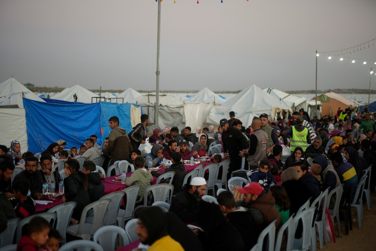 يتجمع فلسطينيون نازحون لتناول وجبة الإفطار، وهي وجبة كسر الصيام، خلال شهر رمضان المبارك في مخيم خيام يؤويهم، بحي الزهراء وسط قطاع غزة، يوم السبت 21 فبراير/شباط 2026. تصوير: عمر أشتوي