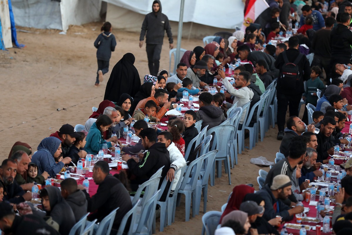 يتجمع فلسطينيون نازحون لتناول وجبة الإفطار، وهي وجبة كسر الصيام، خلال شهر رمضان المبارك في مخيم خيام يؤويهم، بحي الزهراء وسط قطاع غزة، يوم السبت 21 فبراير/شباط 2026. تصوير: عمر أشتوي