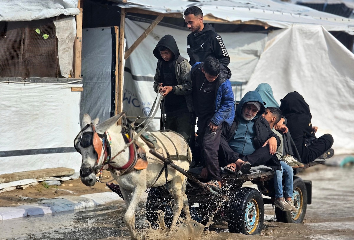 يحاول الفلسطينيون التنقل بعد أن غمرت مياه الأمطار الشوارع وخيام النازحين في خان يونس، جنوب قطاع غزة، في 24 فبراير/شباط 2026. وقد دُمرت البنية التحتية في قطاع غزة على نطاق واسع جراء الحرب والهجمات الإسرائيلية. (صورة: طارق محمد)