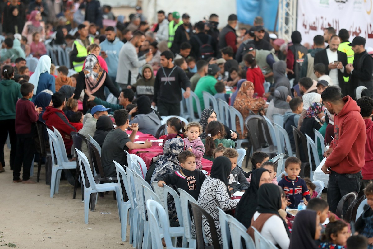يتجمع فلسطينيون نازحون لتناول وجبة الإفطار، وهي وجبة كسر الصيام، خلال شهر رمضان المبارك في مخيم خيام يؤويهم، بحي الزهراء وسط قطاع غزة، يوم السبت 21 فبراير/شباط 2026. تصوير: عمر أشتوي