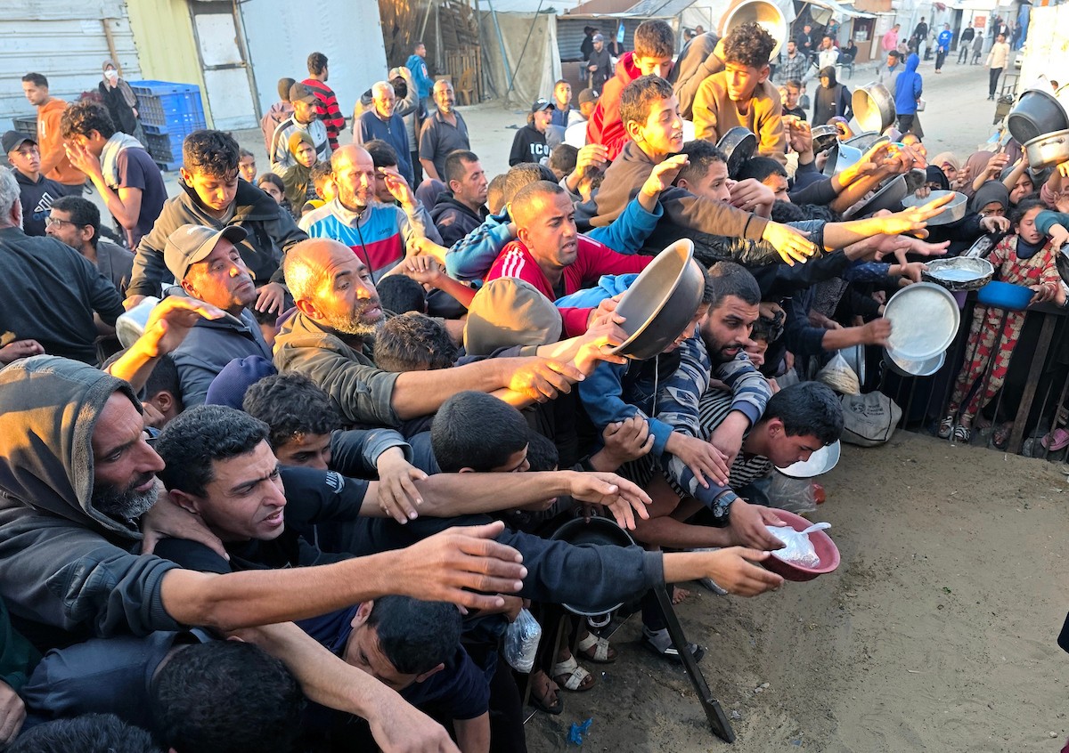 فلسطينيون نازحون يكافحون للحصول على طعام مُتبرع به للإفطار، وجبة كسر الصيام، في اليوم الرابع من شهر رمضان المبارك في مطبخ مجتمعي في خان يونس، قطاع غزة، 21 فبراير/شباط 2026. تصوير: طارق محمد/(APA Images)