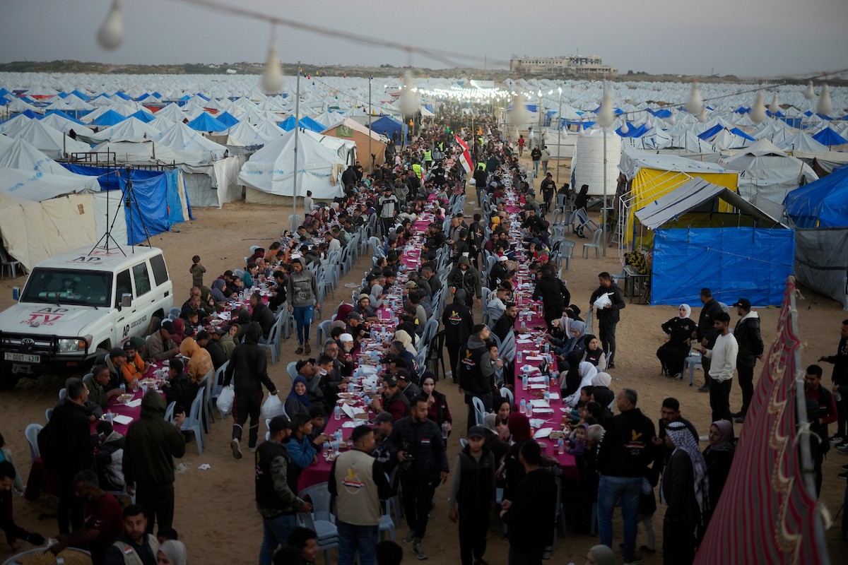 يتجمع فلسطينيون نازحون لتناول وجبة الإفطار، وهي وجبة كسر الصيام، خلال شهر رمضان المبارك في مخيم خيام يؤويهم، بحي الزهراء وسط قطاع غزة، يوم السبت 21 فبراير/شباط 2026. تصوير: عمر أشتوي