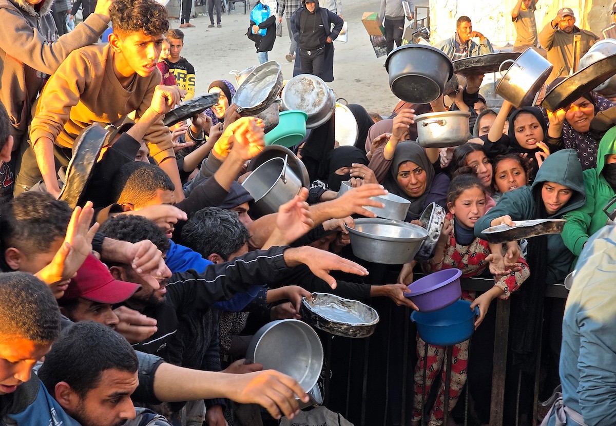 فلسطينيون نازحون يكافحون للحصول على طعام مُتبرع به للإفطار، وجبة كسر الصيام، في اليوم الرابع من شهر رمضان المبارك في مطبخ مجتمعي في خان يونس، قطاع غزة، 21 فبراير/شباط 2026. تصوير: طارق محمد/(APA Images)