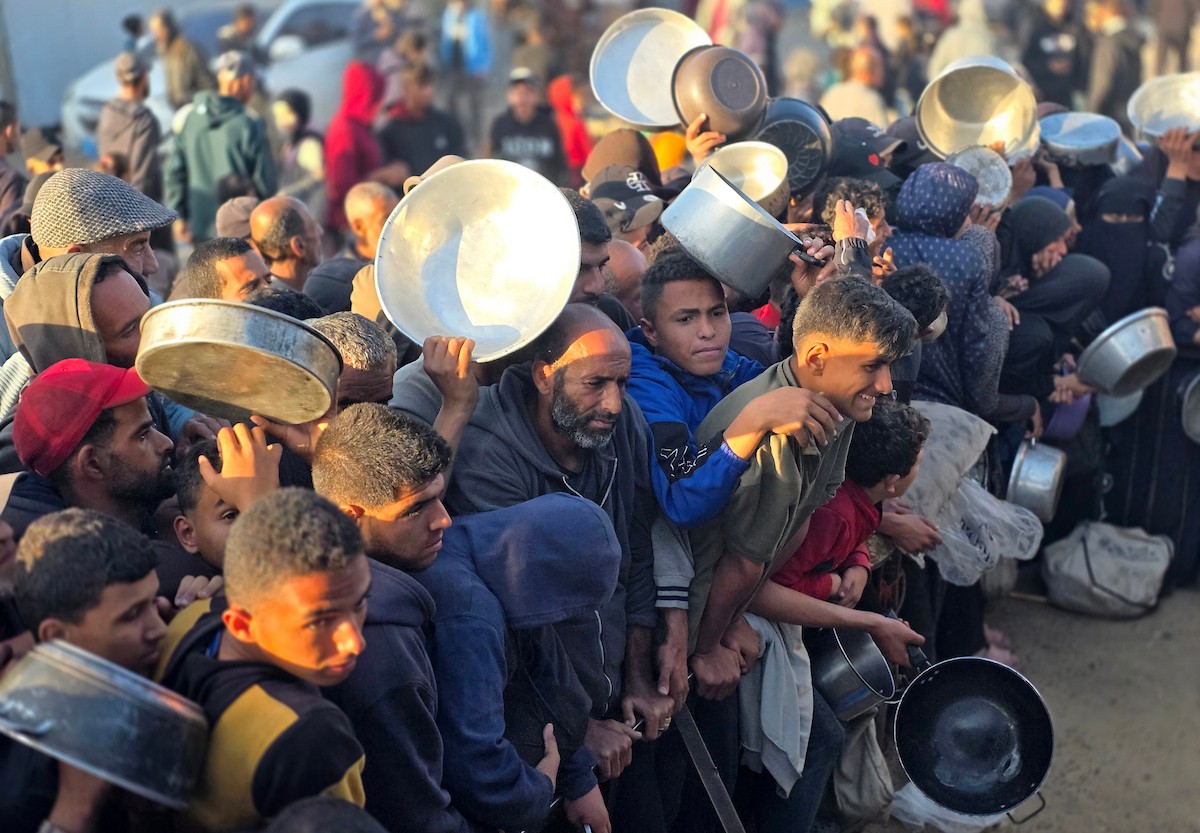 فلسطينيون نازحون يكافحون للحصول على طعام مُتبرع به للإفطار، وجبة كسر الصيام، في اليوم الرابع من شهر رمضان المبارك في مطبخ مجتمعي في خان يونس، قطاع غزة، 21 فبراير/شباط 2026. تصوير: طارق محمد/(APA Images)