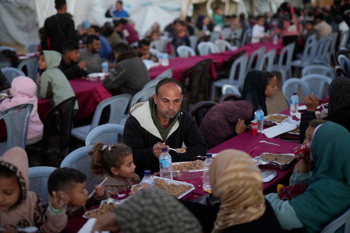 يتجمع فلسطينيون نازحون لتناول وجبة الإفطار، وهي وجبة كسر الصيام، خلال شهر رمضان المبارك في مخيم خيام يؤويهم، بحي الزهراء وسط قطاع غزة، يوم السبت 21 فبراير/شباط 2026. تصوير: عمر أشتوي