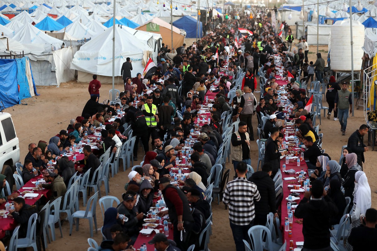 يتجمع فلسطينيون نازحون لتناول وجبة الإفطار، وهي وجبة كسر الصيام، خلال شهر رمضان المبارك في مخيم خيام يؤويهم، بحي الزهراء وسط قطاع غزة، يوم السبت 21 فبراير/شباط 2026. تصوير: عمر أشتوي