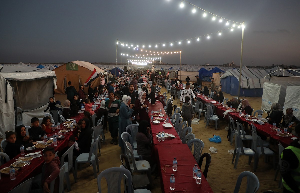 يتجمع فلسطينيون نازحون لتناول وجبة الإفطار، وهي وجبة كسر الصيام، خلال شهر رمضان المبارك في مخيم خيام يؤويهم، بحي الزهراء وسط قطاع غزة، يوم السبت 21 فبراير/شباط 2026. تصوير: عمر أشتوي