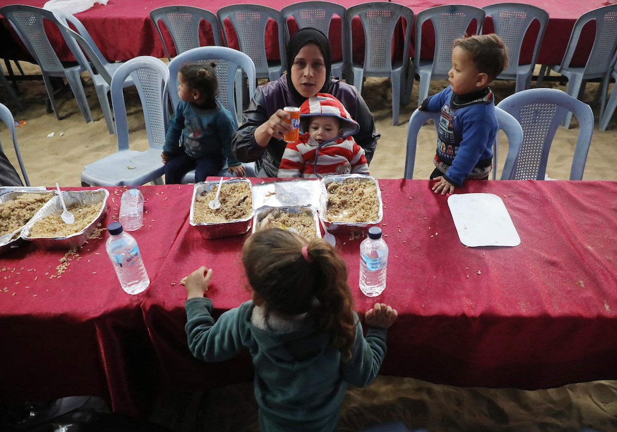 يتجمع فلسطينيون نازحون لتناول وجبة الإفطار، وهي وجبة كسر الصيام، خلال شهر رمضان المبارك في مخيم خيام يؤويهم، بحي الزهراء وسط قطاع غزة، يوم السبت 21 فبراير/شباط 2026. تصوير: عمر أشتوي