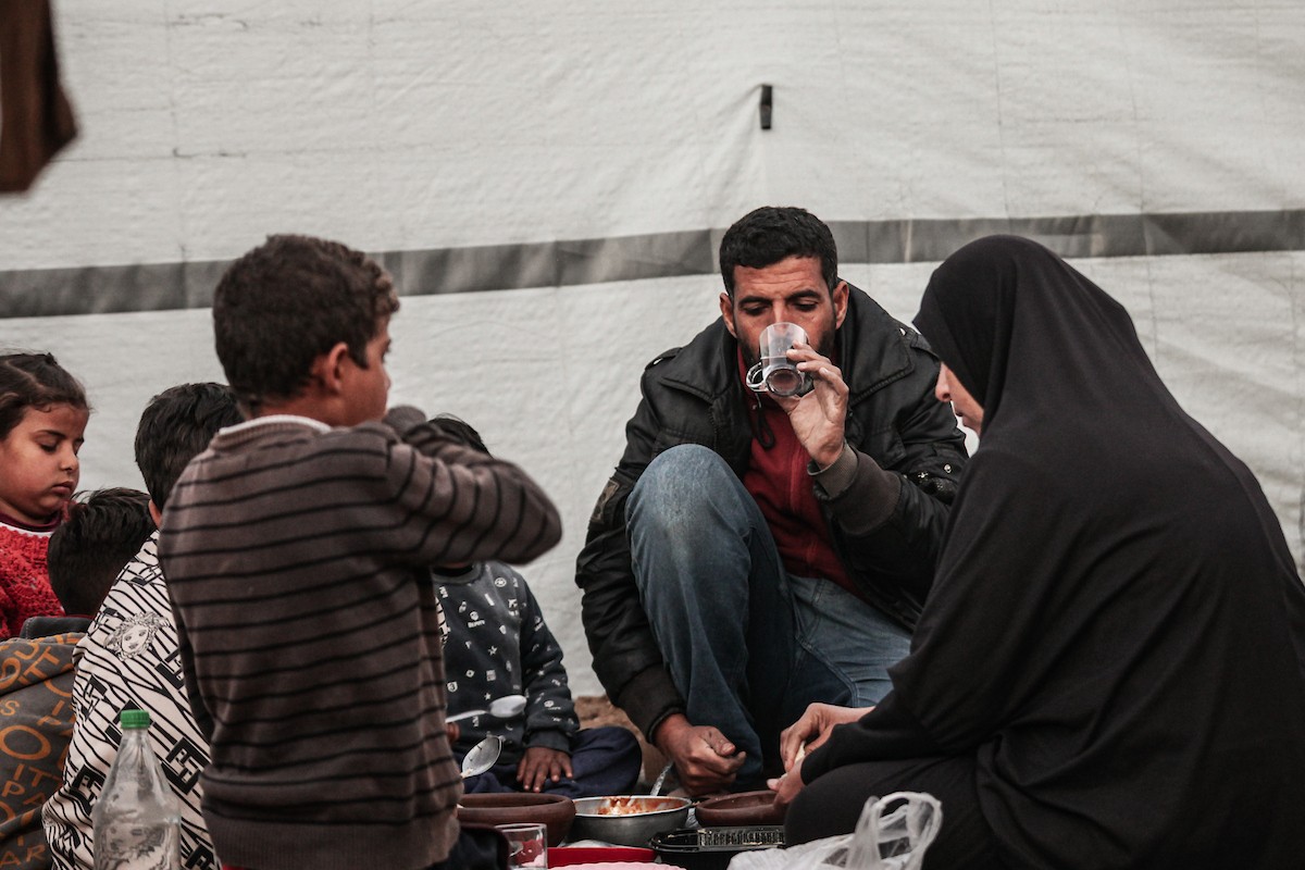 عائلة فلسطينية نازحة تتناول فطورها خلال شهر رمضان داخل خيمة متداعية في مخيم النصيرات للاجئين وسط قطاع غزة. تواجه العائلات النازحة ظروفًا معيشية قاسية نتيجة الحرب، مع انعدام الدخل ونقص حاد في المساعدات الإنسانية، 26 فبراير/شباط 2026. تصوير: معز صالحي
