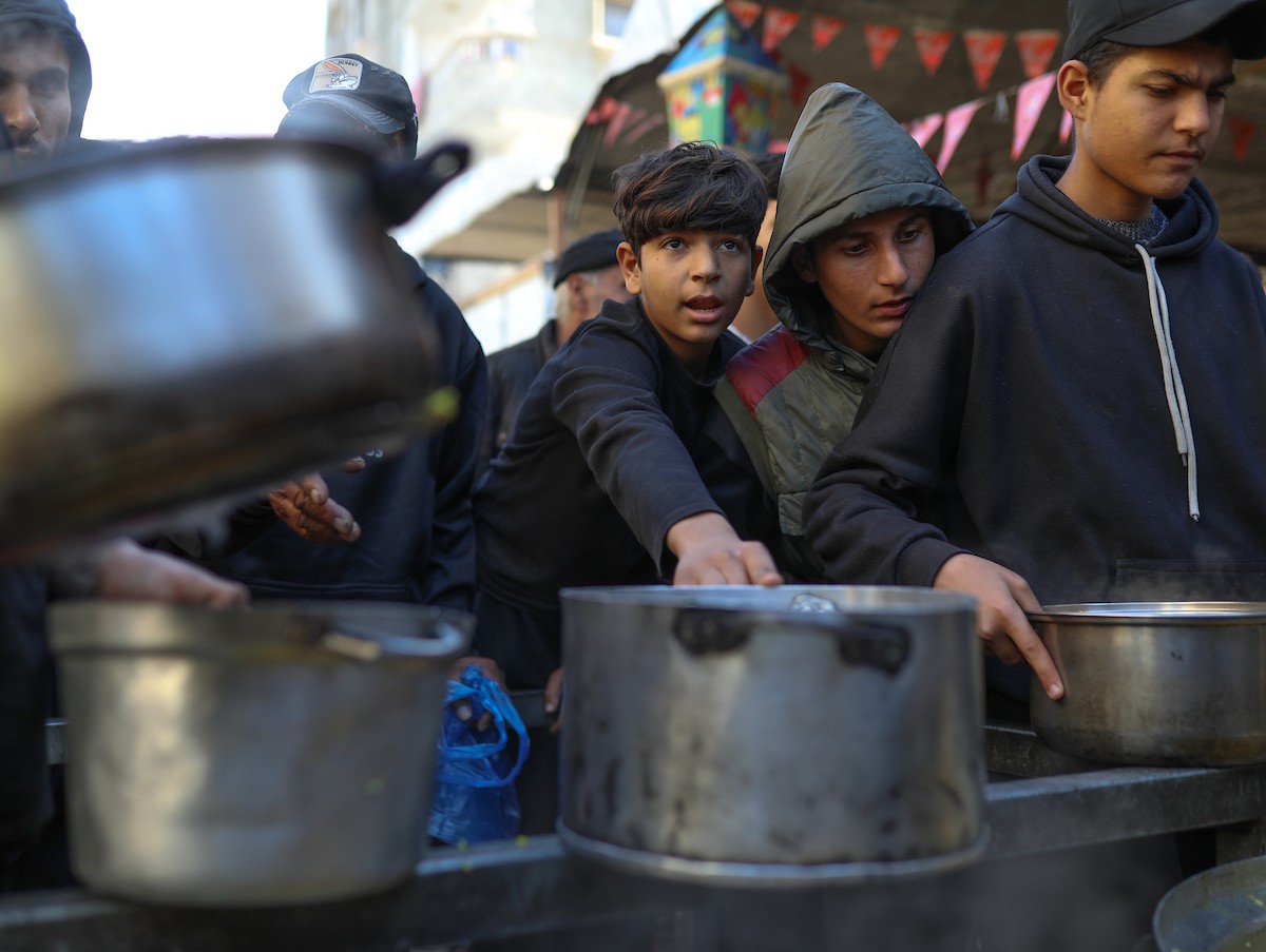 يتجمع فلسطينيون نازحون لتناول وجبة إفطارهم الرمضانية في مطبخ خيري بمخيم النصيرات للاجئين وسط قطاع غزة، في 24 فبراير/شباط 2026. ويواجه النازحون ظروفًا معيشية قاسية نتيجة انعدام الدخل ونقص المساعدات الإنسانية. (صورة: رمزي أبو عامر / apaimages)