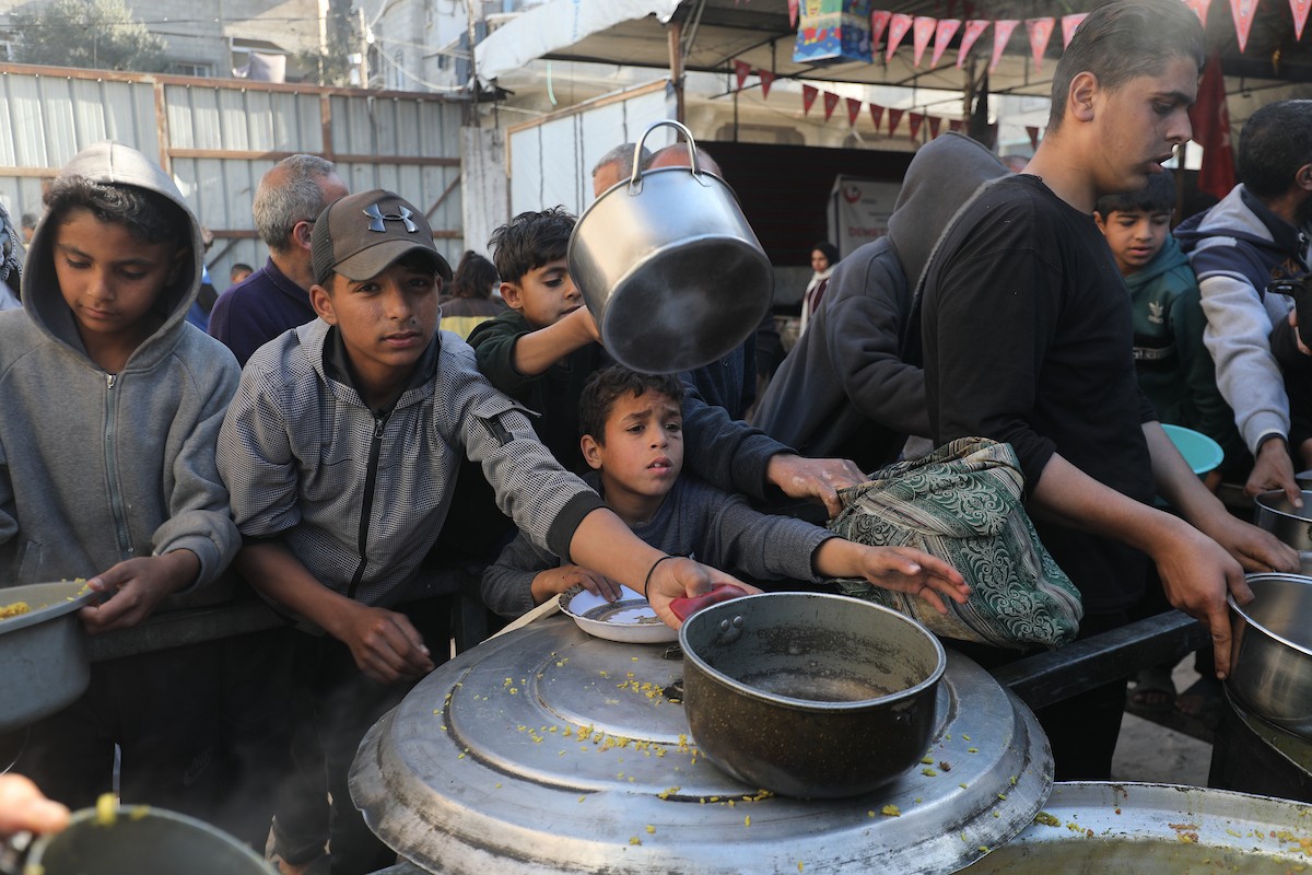 يتجمع فلسطينيون لتناول وجبة ساخنة وزعتها إحدى الجمعيات الخيرية، وسط أزمة غذائية مستمرة بسبب محدودية المساعدات الإنسانية خلال شهر رمضان في مخيم النصيرات للاجئين وسط قطاع غزة. ٢٣ فبرايرشباط ٢٠٢٦. تصوير معز صالحي