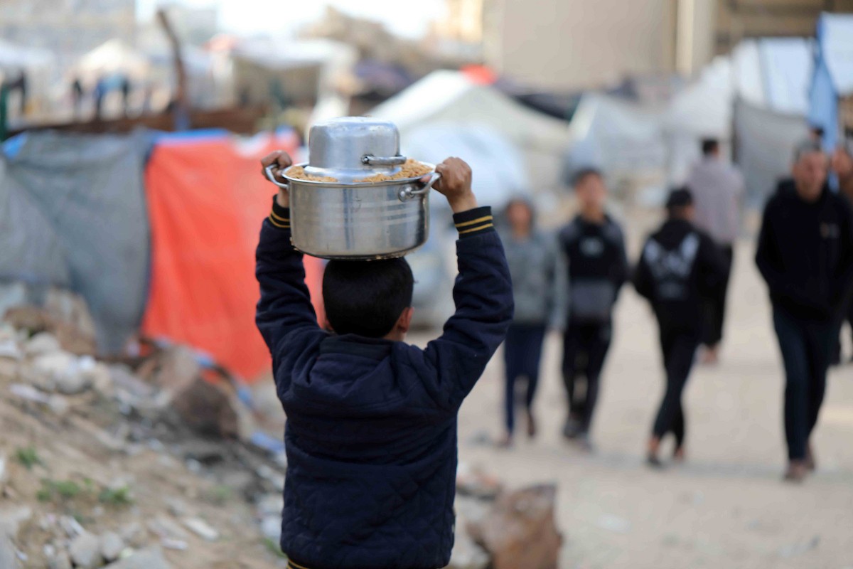 تجمع فلسطينيون نازحون، بينهم أطفال ونساء، حاملين أوعية طعام لتلقي وجبات ساخنة وزعتها جمعيات خيرية قبل الإفطار في مدينة غزة في 27 فبراير/شباط 2026.صورة: عمر أشتوي