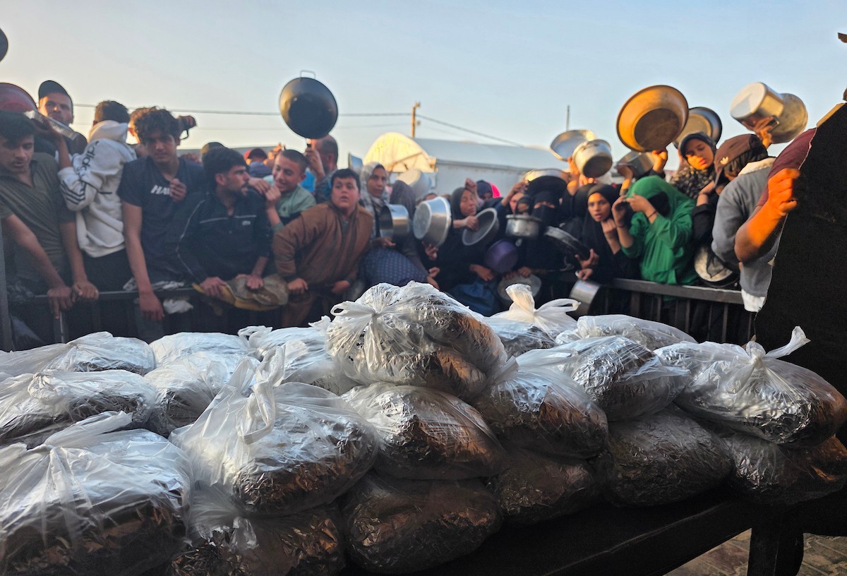 فلسطينيون نازحون يكافحون للحصول على طعام مُتبرع به للإفطار، وجبة كسر الصيام، في اليوم الرابع من شهر رمضان المبارك في مطبخ مجتمعي في خان يونس، قطاع غزة، 21 فبراير/شباط 2026. تصوير: طارق محمد/(APA Images)