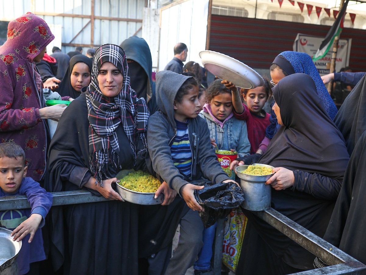 يتجمع فلسطينيون نازحون لتناول وجبة إفطارهم الرمضانية في مطبخ خيري بمخيم النصيرات للاجئين وسط قطاع غزة، في 24 فبراير/شباط 2026. ويواجه النازحون ظروفًا معيشية قاسية نتيجة انعدام الدخل ونقص المساعدات الإنسانية. (صورة: رمزي أبو عامر / apaimages)