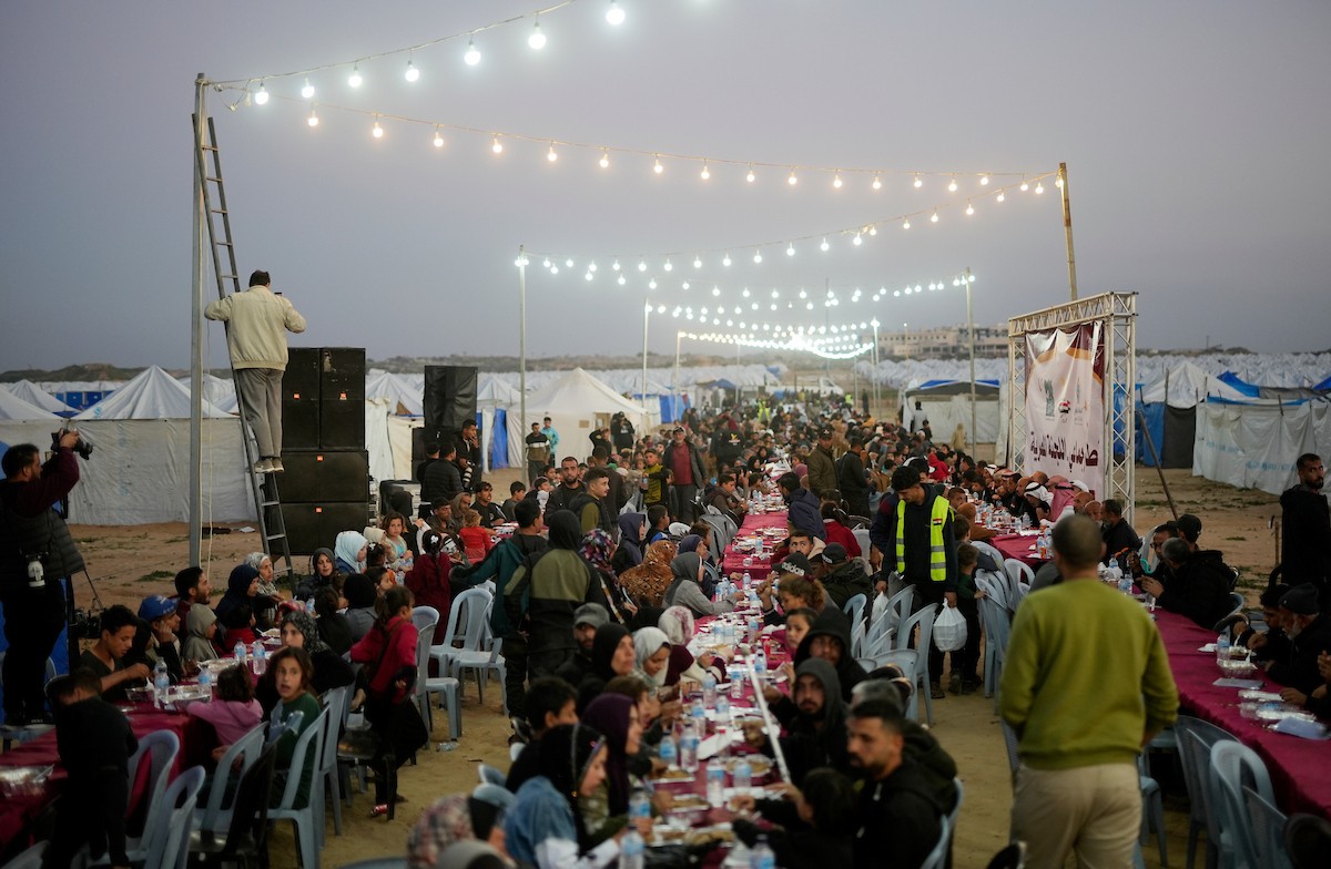 يتجمع فلسطينيون نازحون لتناول وجبة الإفطار، وهي وجبة كسر الصيام، خلال شهر رمضان المبارك في مخيم خيام يؤويهم، بحي الزهراء وسط قطاع غزة، يوم السبت 21 فبراير/شباط 2026. تصوير: عمر أشتوي