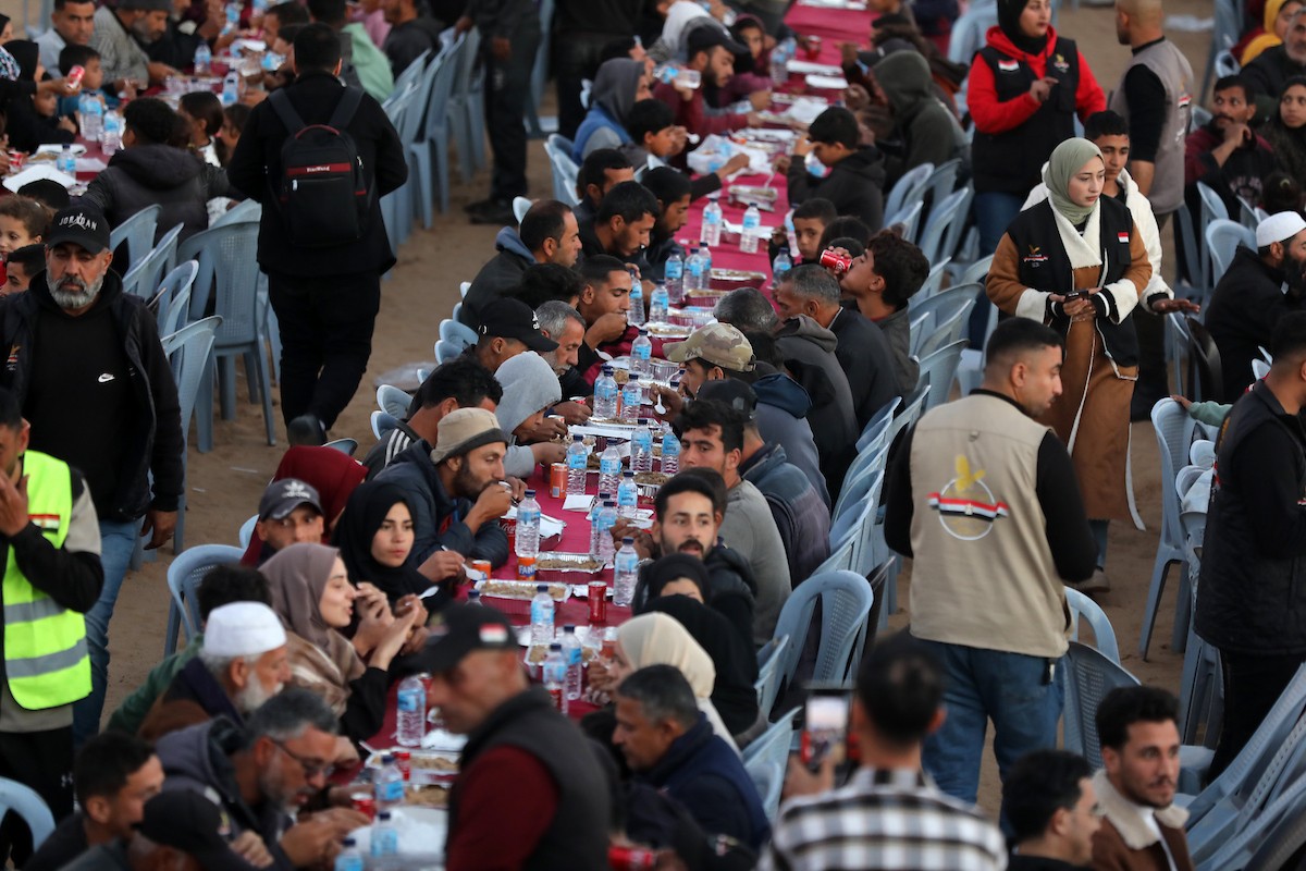 يتجمع فلسطينيون نازحون لتناول وجبة الإفطار، وهي وجبة كسر الصيام، خلال شهر رمضان المبارك في مخيم خيام يؤويهم، بحي الزهراء وسط قطاع غزة، يوم السبت 21 فبراير/شباط 2026. تصوير: عمر أشتوي