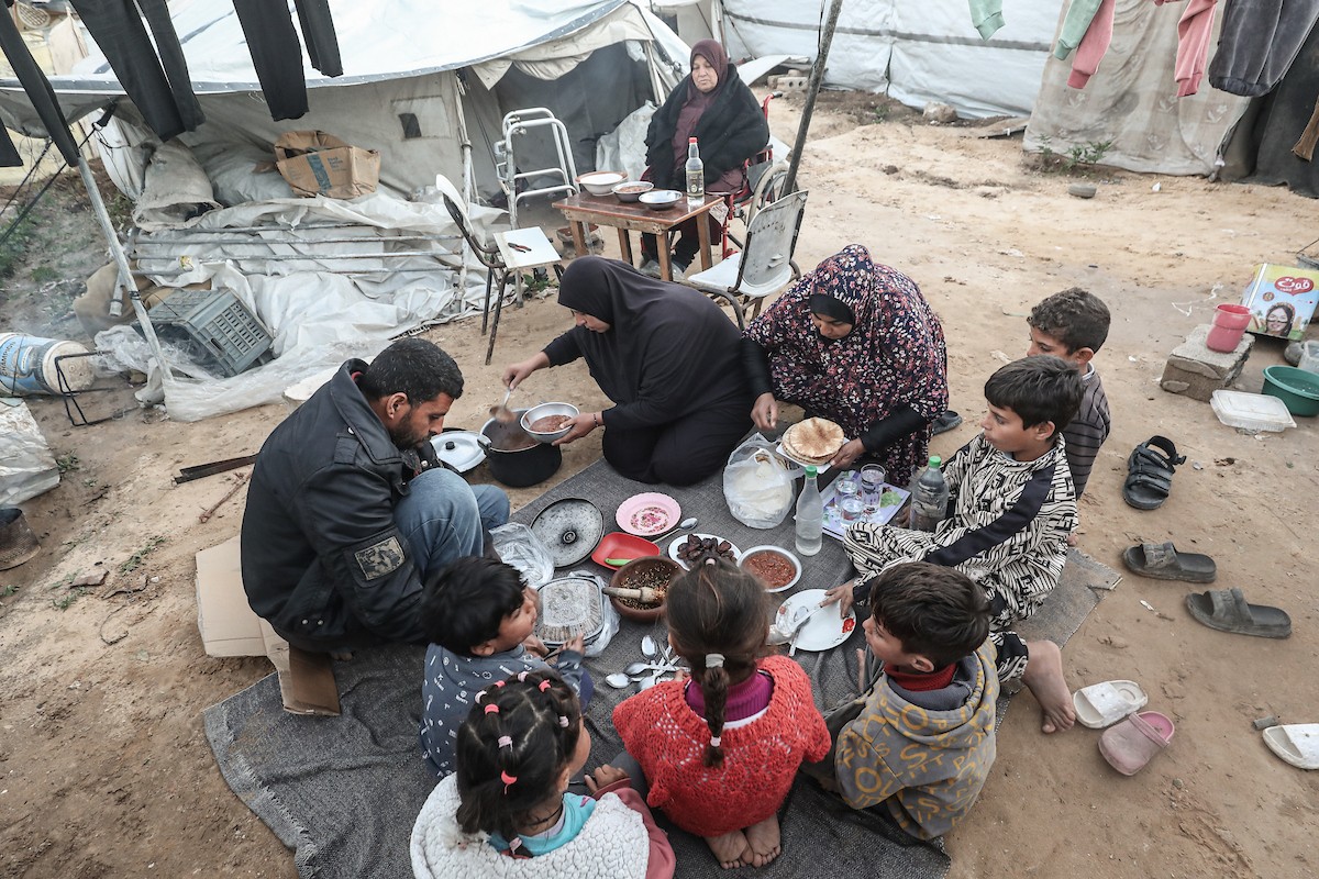 عائلة فلسطينية نازحة تتناول فطورها خلال شهر رمضان داخل خيمة متداعية في مخيم النصيرات للاجئين وسط قطاع غزة. تواجه العائلات النازحة ظروفًا معيشية قاسية نتيجة الحرب، مع انعدام الدخل ونقص حاد في المساعدات الإنسانية، 26 فبراير/شباط 2026. تصوير: معز صالحي