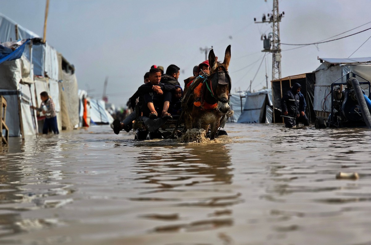 يحاول الفلسطينيون التنقل بعد أن غمرت مياه الأمطار الشوارع وخيام النازحين في خان يونس، جنوب قطاع غزة، في 24 فبراير/شباط 2026. وقد دُمرت البنية التحتية في قطاع غزة على نطاق واسع جراء الحرب والهجمات الإسرائيلية. (صورة: طارق محمد)