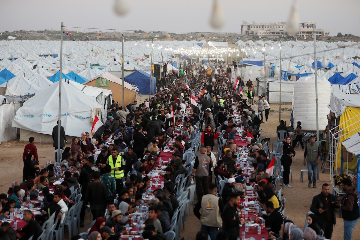 يتجمع فلسطينيون نازحون لتناول وجبة الإفطار، وهي وجبة كسر الصيام، خلال شهر رمضان المبارك في مخيم خيام يؤويهم، بحي الزهراء وسط قطاع غزة، يوم السبت 21 فبراير/شباط 2026. تصوير: عمر أشتوي