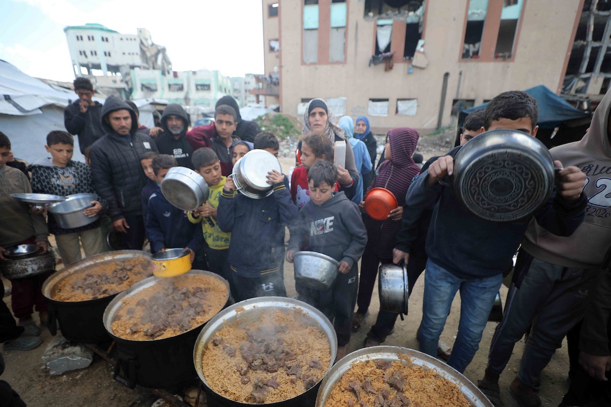 تجمع فلسطينيون نازحون، بينهم أطفال ونساء، حاملين أوعية طعام لتلقي وجبات ساخنة وزعتها جمعيات خيرية قبل الإفطار في مدينة غزة في 27 فبراير/شباط 2026.صورة: عمر أشتوي