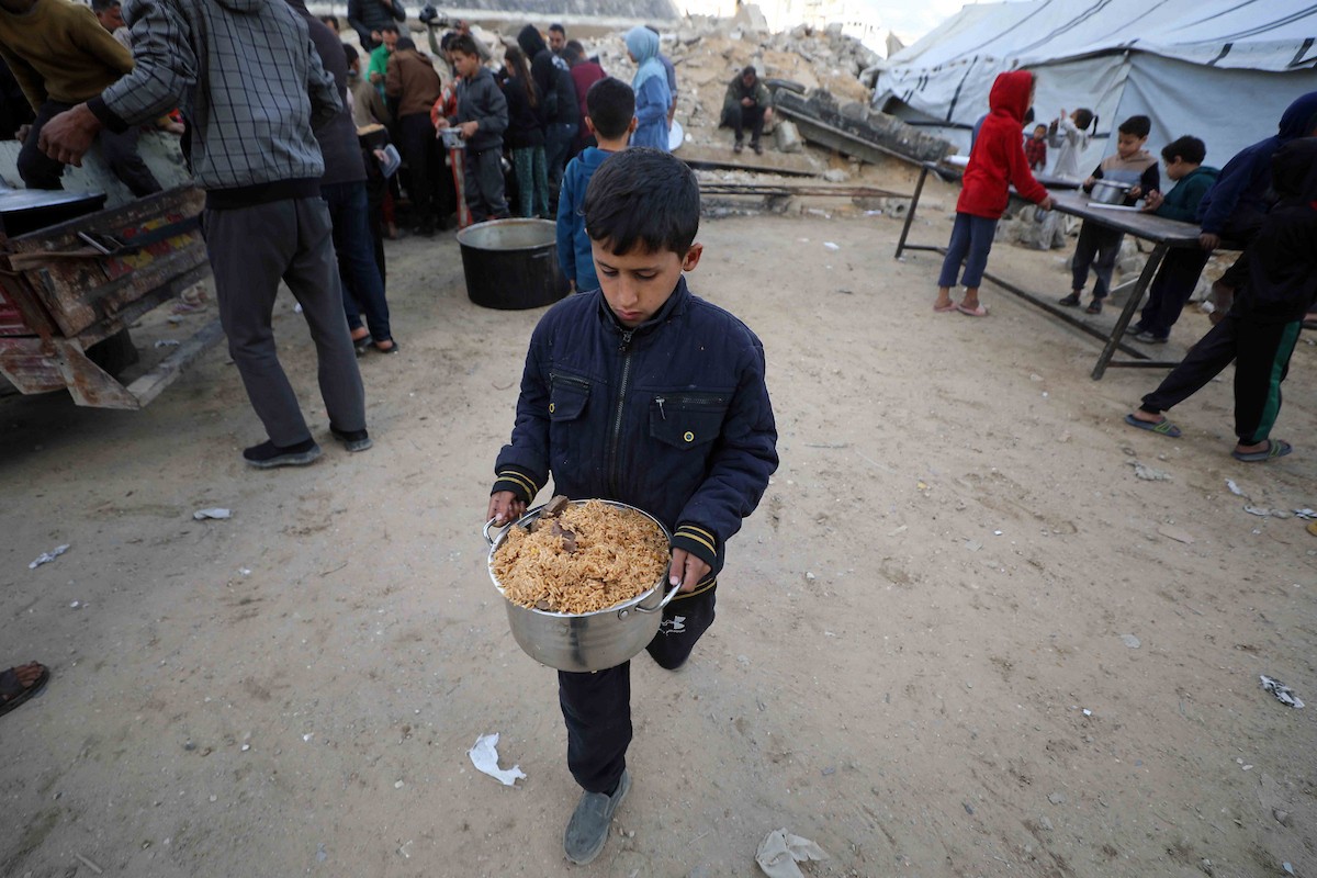 تجمع فلسطينيون نازحون، بينهم أطفال ونساء، حاملين أوعية طعام لتلقي وجبات ساخنة وزعتها جمعيات خيرية قبل الإفطار في مدينة غزة في 27 فبراير/شباط 2026.صورة: عمر أشتوي