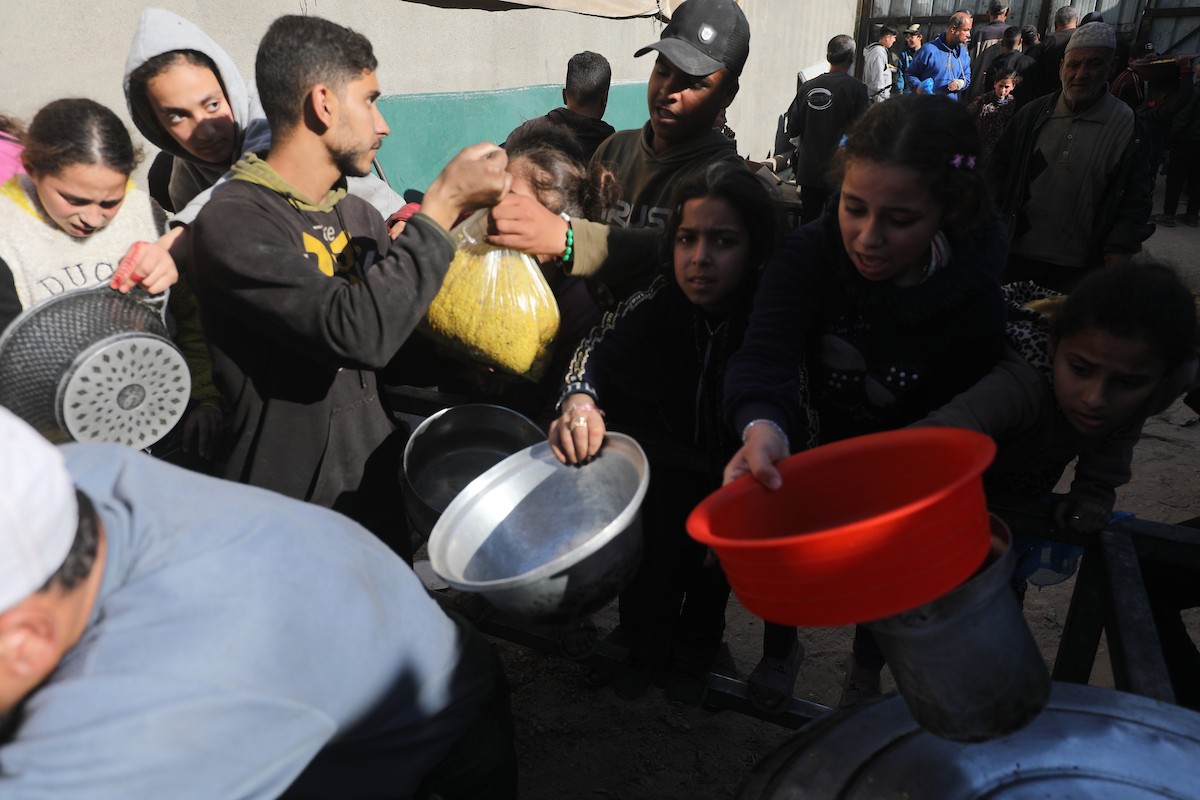 يتجمع فلسطينيون لتناول وجبة ساخنة وزعتها إحدى الجمعيات الخيرية، وسط أزمة غذائية مستمرة بسبب محدودية المساعدات الإنسانية خلال شهر رمضان في مخيم النصيرات للاجئين وسط قطاع غزة. ٢٣ فبرايرشباط ٢٠٢٦. تصوير معز صالحي
