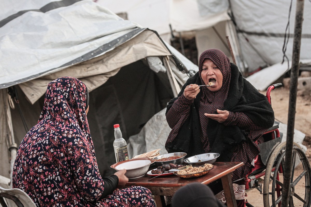 عائلة فلسطينية نازحة تتناول فطورها خلال شهر رمضان داخل خيمة متداعية في مخيم النصيرات للاجئين وسط قطاع غزة. تواجه العائلات النازحة ظروفًا معيشية قاسية نتيجة الحرب، مع انعدام الدخل ونقص حاد في المساعدات الإنسانية، 26 فبراير/شباط 2026. تصوير: معز صالحي