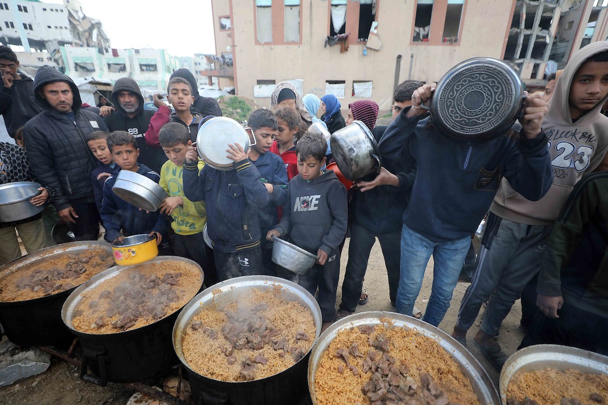 تجمع فلسطينيون نازحون، بينهم أطفال ونساء، حاملين أوعية طعام لتلقي وجبات ساخنة وزعتها جمعيات خيرية قبل الإفطار في مدينة غزة في 27 فبراير/شباط 2026.صورة: عمر أشتوي