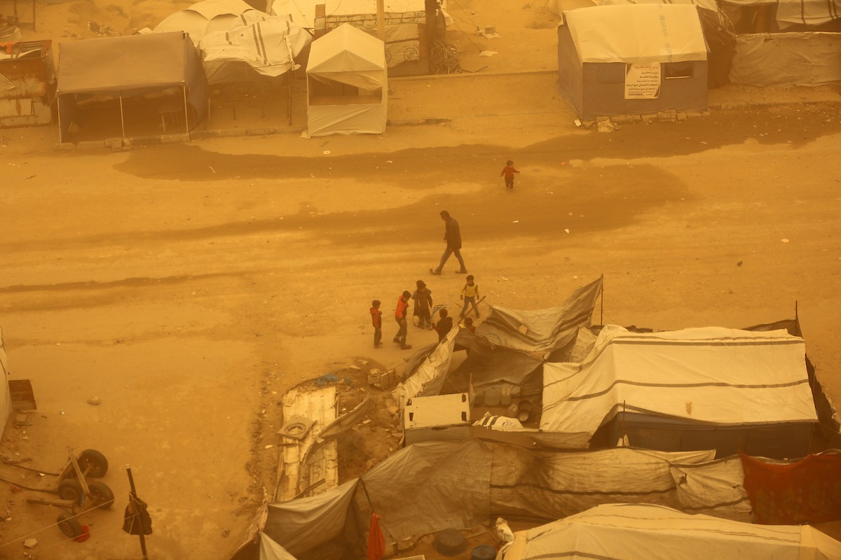 فلسطينيون يسيرون وسط عاصفة رملية في مخيم خيام يؤوي فلسطينيين نزحوا خلال العدوان الإسرائيلي الذي استمر عامين، في خان يونس جنوب قطاع غزة، 14 مارس/آذار 2026. تصوير: طارق محم