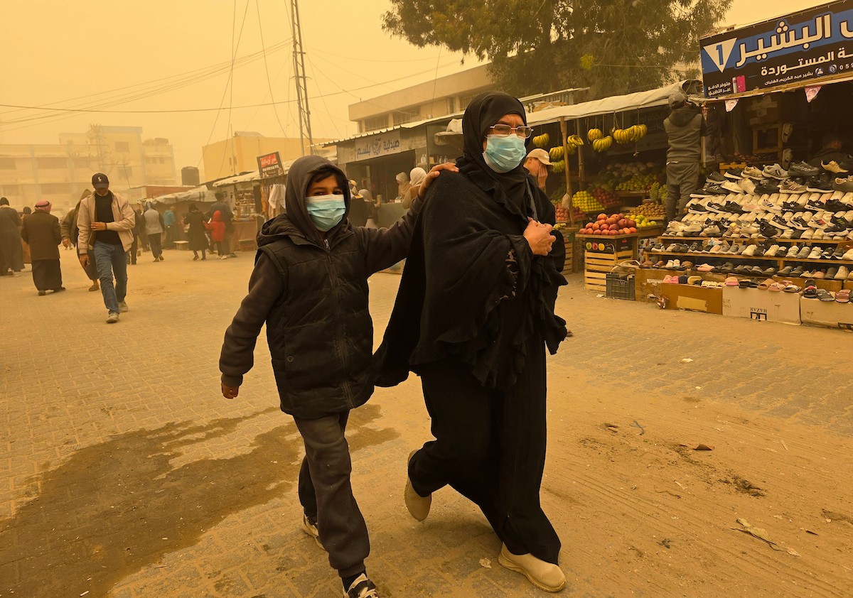 فلسطينيون يسيرون وسط عاصفة رملية في مخيم خيام يؤوي فلسطينيين نزحوا خلال العدوان الإسرائيلي الذي استمر عامين، في خان يونس جنوب قطاع غزة، 14 مارس/آذار 2026. تصوير: طارق محم