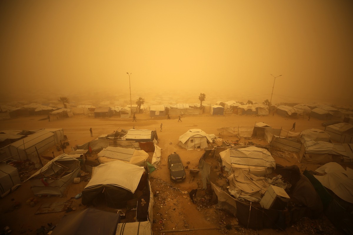 فلسطينيون يسيرون وسط عاصفة رملية في مخيم خيام يؤوي فلسطينيين نزحوا خلال العدوان الإسرائيلي الذي استمر عامين، في مدينة غزة، 14 مارس/آذار 2026. صورة: عمر أشتوي