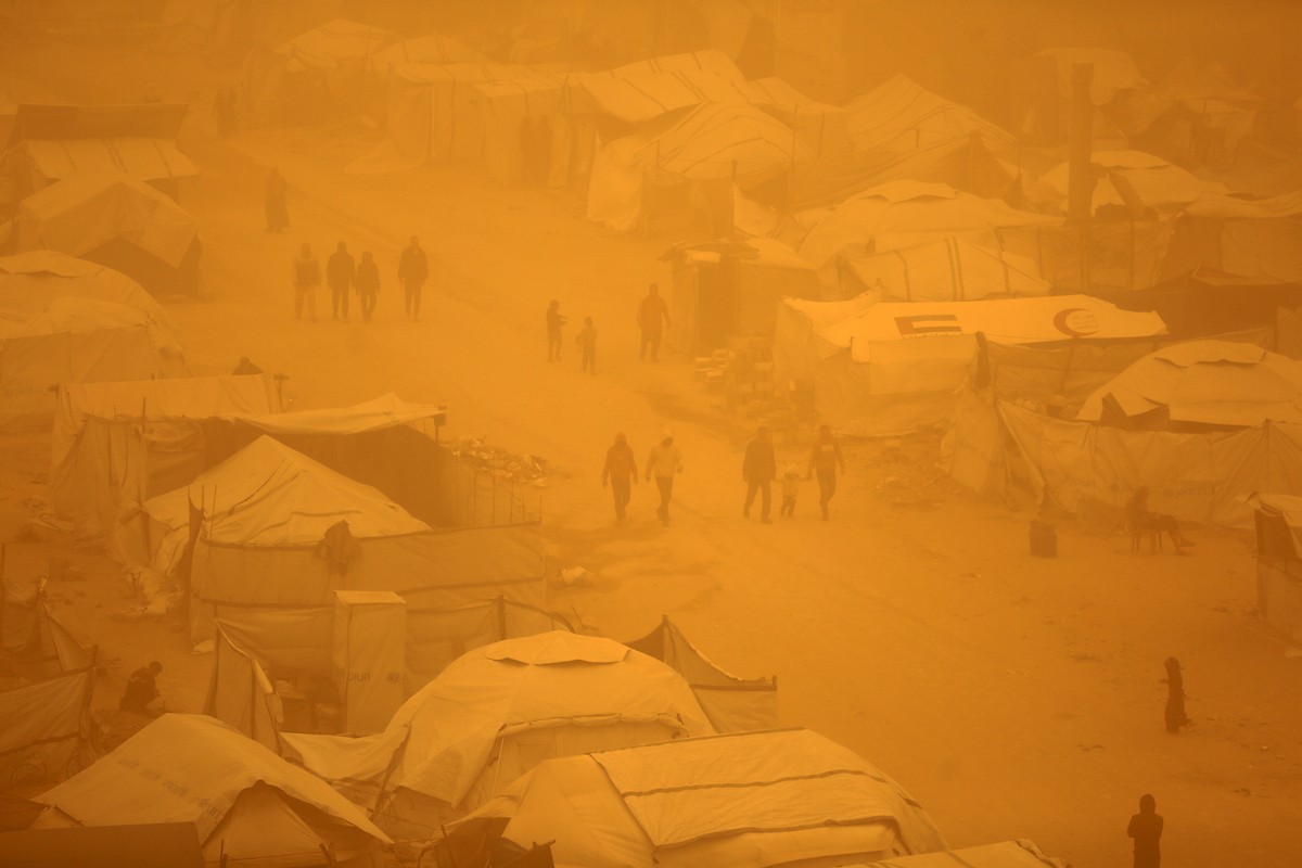 فلسطينيون يسيرون وسط عاصفة رملية في مخيم خيام يؤوي فلسطينيين نزحوا خلال العدوان الإسرائيلي الذي استمر عامين، في مدينة غزة، 14 مارس/آذار 2026. صورة: عمر أشتوي