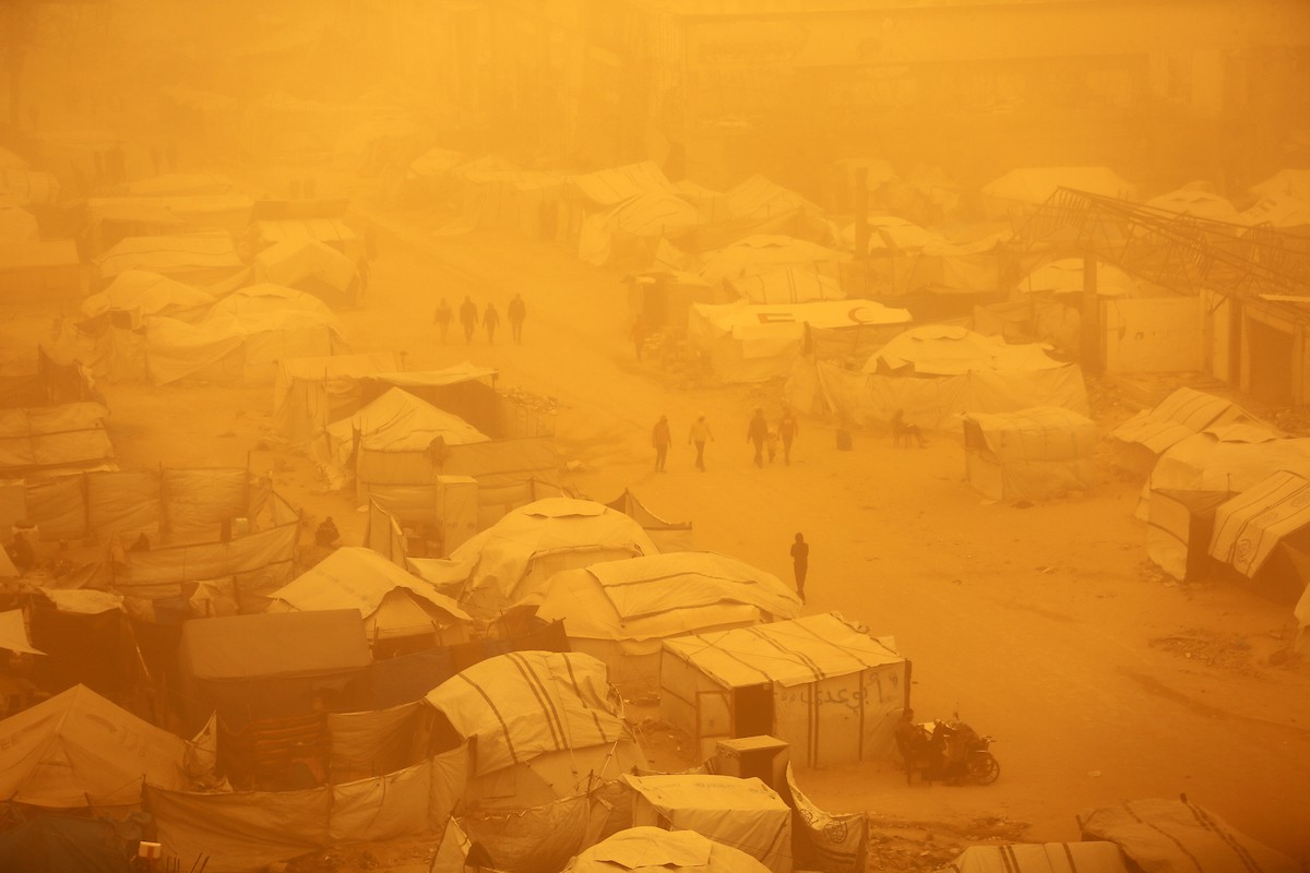 فلسطينيون يسيرون وسط عاصفة رملية في مخيم خيام يؤوي فلسطينيين نزحوا خلال العدوان الإسرائيلي الذي استمر عامين، في مدينة غزة، 14 مارس/آذار 2026. صورة: عمر أشتوي