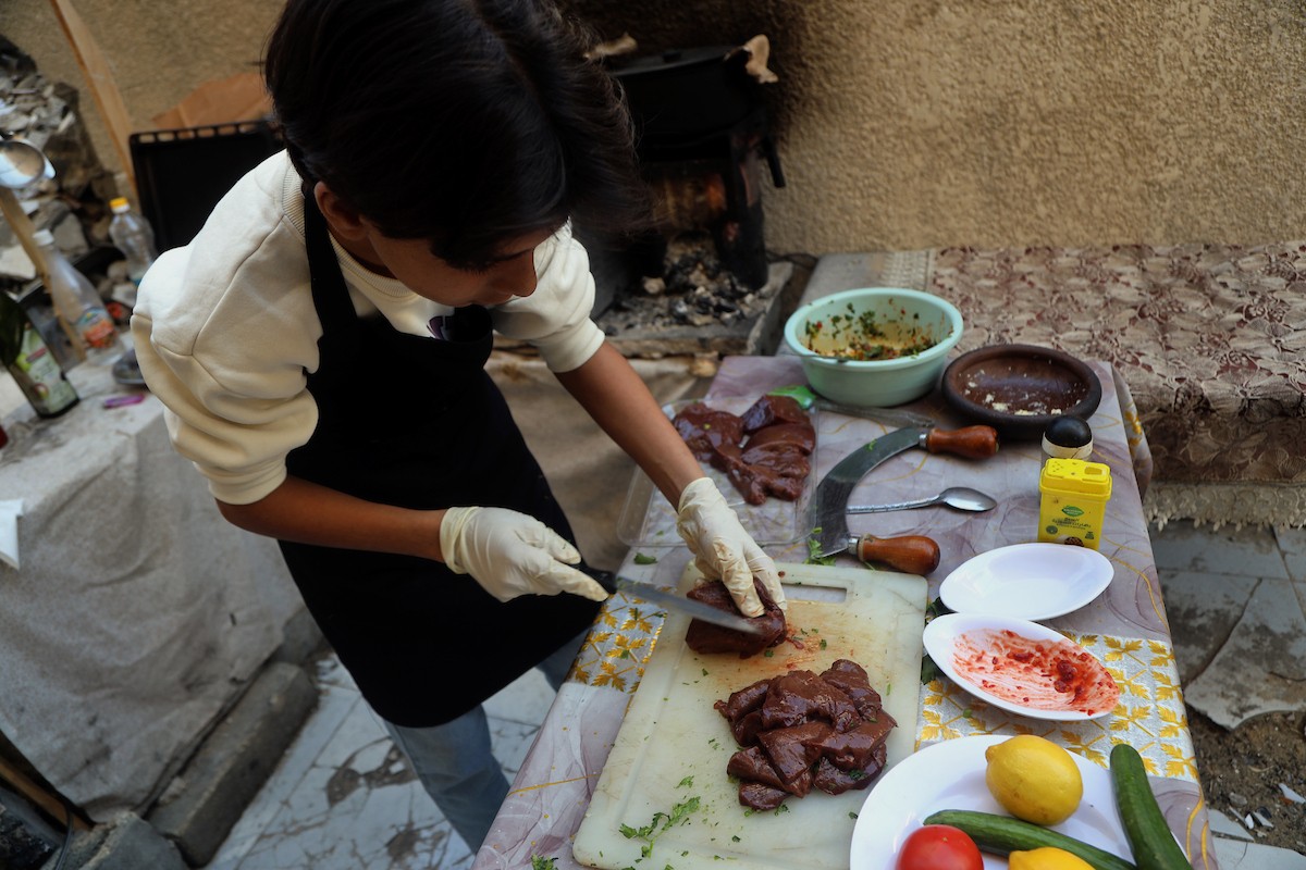 ياسر عياد، فتى فلسطيني يبلغ من العمر أربعة عشر عامًا، يمارس مهاراته في الطبخ على نار الحطب بجوار أنقاض منزل عائلته المدمر في مدينة غزة. غزة، 10 أبريل/نيسان 2026. تصوير: محمد الأسود