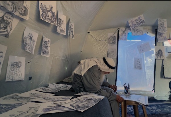 محمد زملط، رجل فلسطيني مسنّ اقتلعته الحرب من مخيم جباليا في شمال قطاع غزة، يحمل اليوم ريشته كوسيلة للبقاء، لا للفن فقط. في خيمته المتواضعة بمخيم البريج وسط القطاع، 12 أبريل/نيسان 2026، عدسة: يوسف أبو وطفة