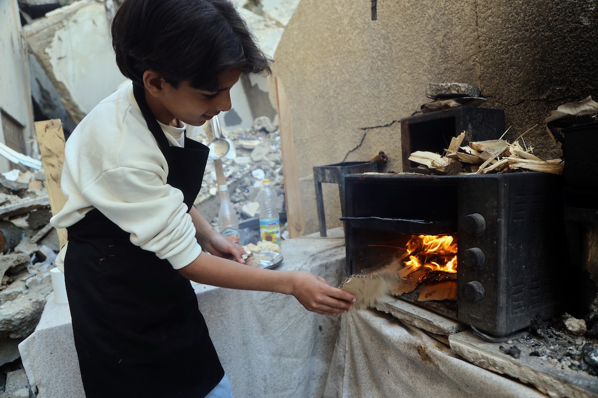ياسر عياد، فتى فلسطيني يبلغ من العمر أربعة عشر عامًا، يمارس مهاراته في الطبخ على نار الحطب بجوار أنقاض منزل عائلته المدمر في مدينة غزة. غزة، 10 أبريل/نيسان 2026. تصوير: محمد الأسود
