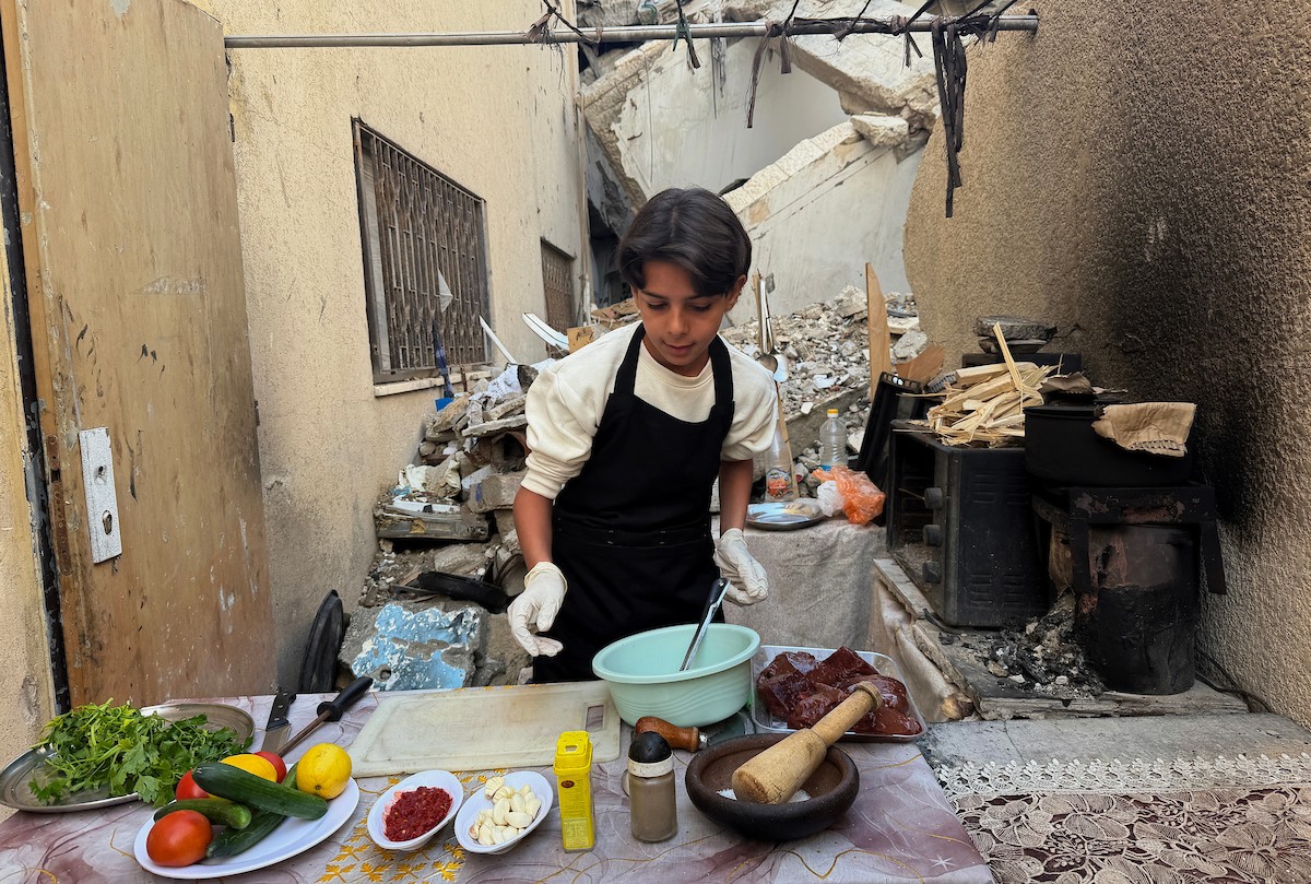 ياسر عياد، فتى فلسطيني يبلغ من العمر أربعة عشر عامًا، يمارس مهاراته في الطبخ على نار الحطب بجوار أنقاض منزل عائلته المدمر في مدينة غزة. غزة، 10 أبريل/نيسان 2026. تصوير: محمد الأسود