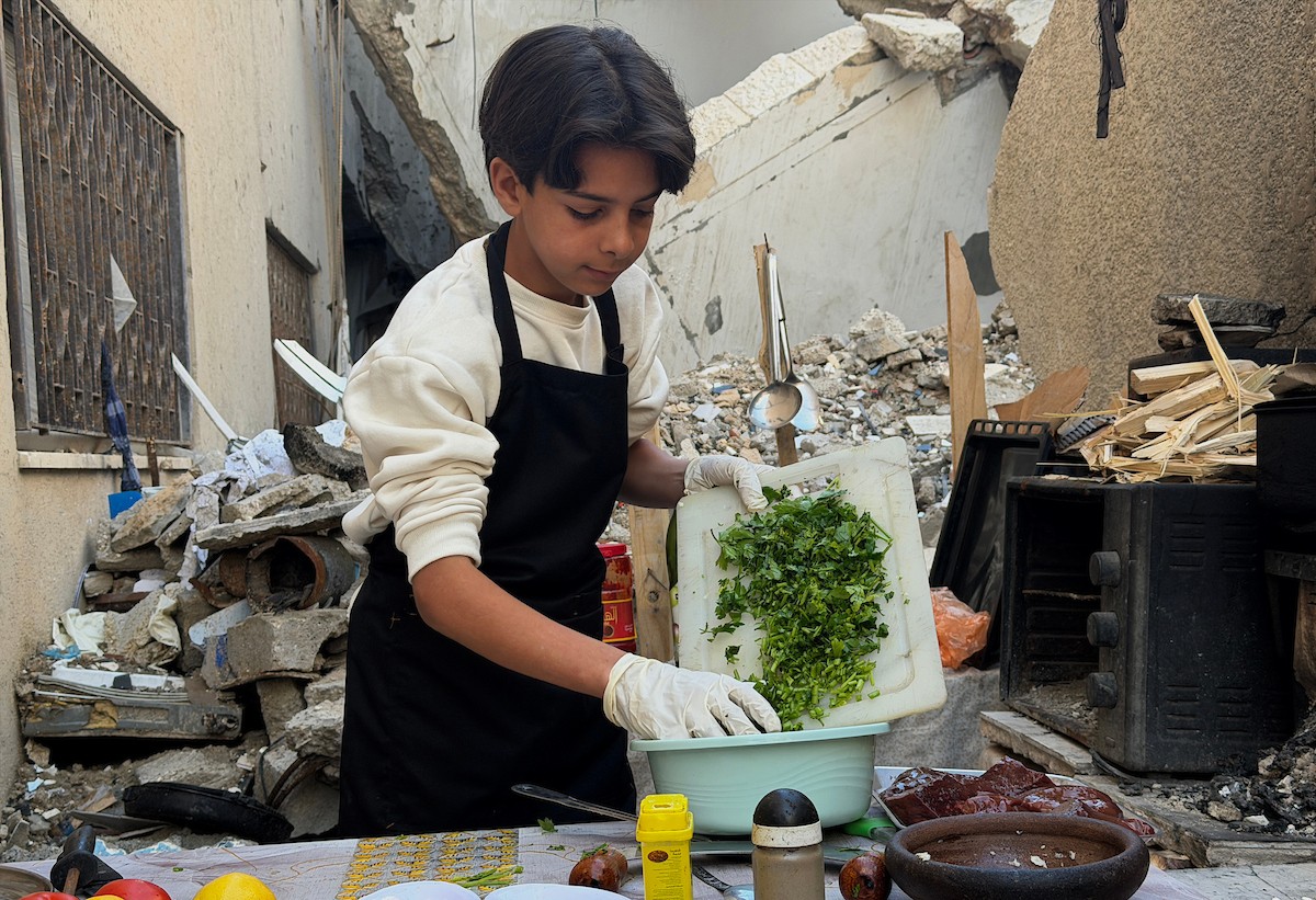 ياسر عياد، فتى فلسطيني يبلغ من العمر أربعة عشر عامًا، يمارس مهاراته في الطبخ على نار الحطب بجوار أنقاض منزل عائلته المدمر في مدينة غزة. غزة، 10 أبريل/نيسان 2026. تصوير: محمد الأسود