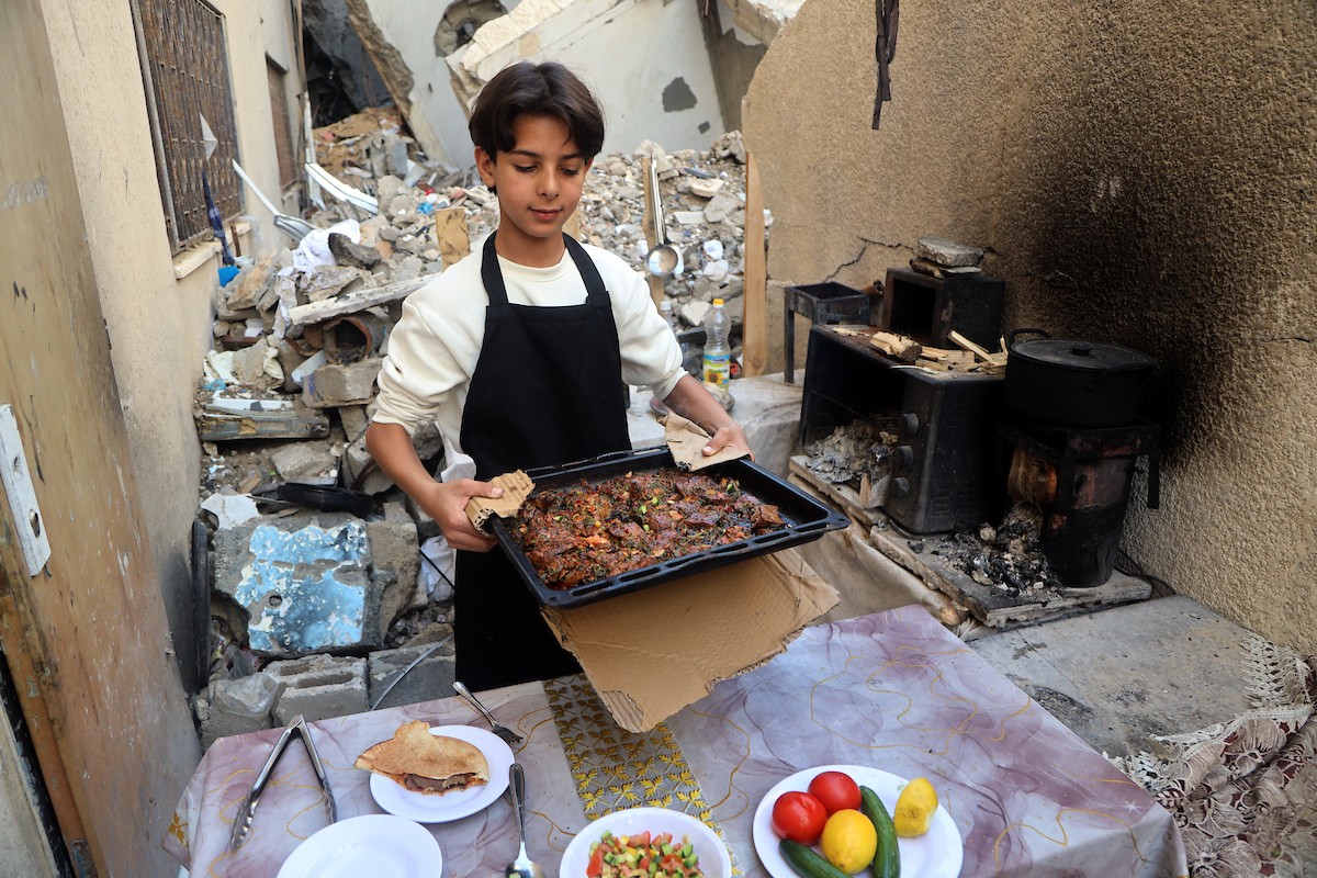ياسر عياد، فتى فلسطيني يبلغ من العمر أربعة عشر عامًا، يمارس مهاراته في الطبخ على نار الحطب بجوار أنقاض منزل عائلته المدمر في مدينة غزة. غزة، 10 أبريل/نيسان 2026. تصوير: محمد الأسود