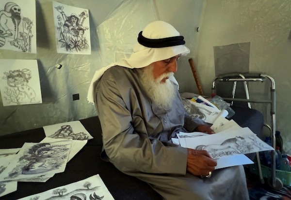 محمد زملط، رجل فلسطيني مسنّ اقتلعته الحرب من مخيم جباليا في شمال قطاع غزة، يحمل اليوم ريشته كوسيلة للبقاء، لا للفن فقط. في خيمته المتواضعة بمخيم البريج وسط القطاع، 12 أبريل/نيسان 2026، عدسة: يوسف أبو وطفة