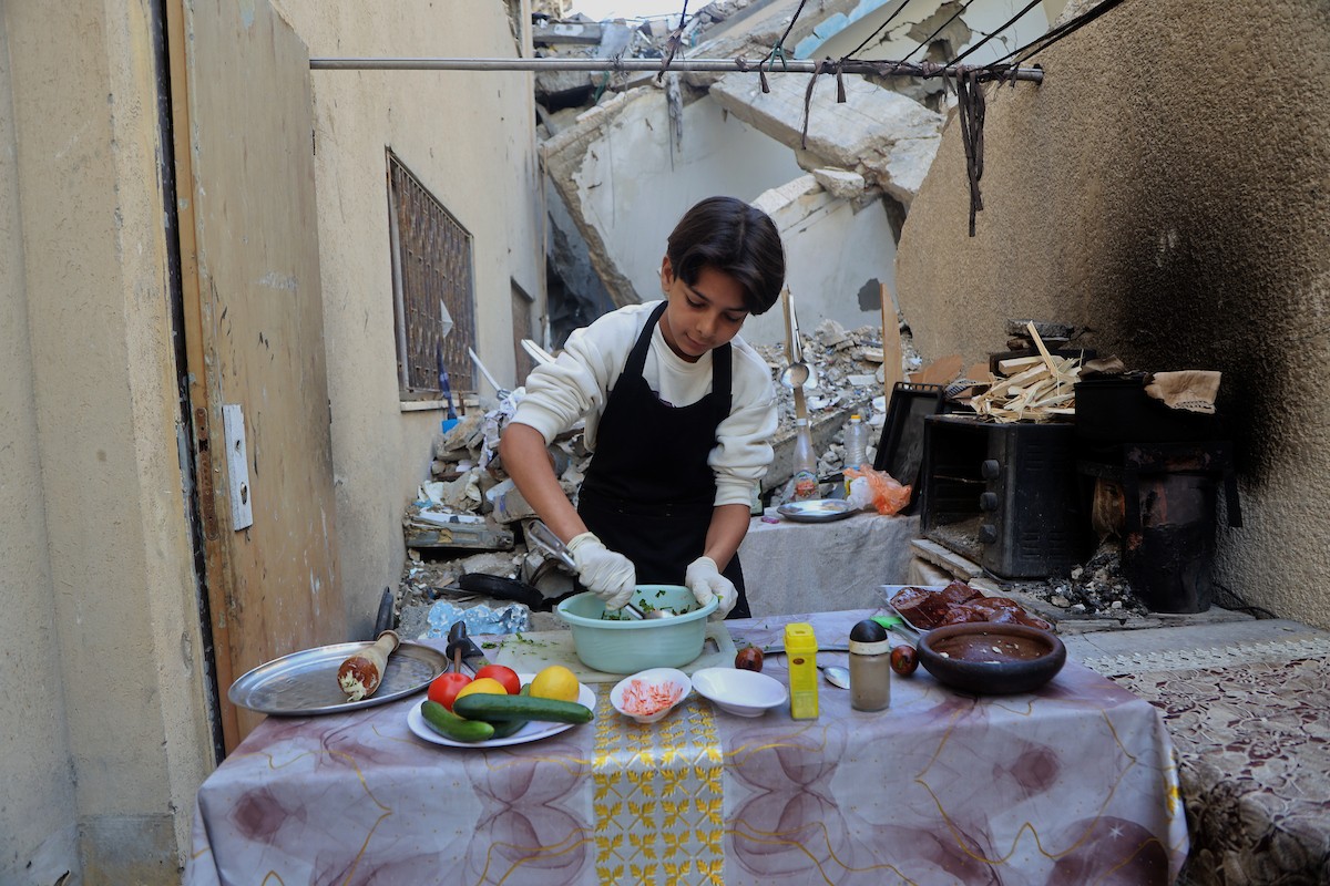 ياسر عياد، فتى فلسطيني يبلغ من العمر أربعة عشر عامًا، يمارس مهاراته في الطبخ على نار الحطب بجوار أنقاض منزل عائلته المدمر في مدينة غزة. غزة، 10 أبريل/نيسان 2026. تصوير: محمد الأسود
