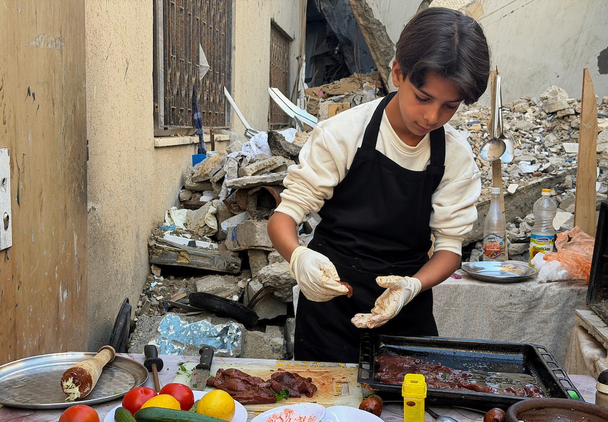 ياسر عياد، فتى فلسطيني يبلغ من العمر أربعة عشر عامًا، يمارس مهاراته في الطبخ على نار الحطب بجوار أنقاض منزل عائلته المدمر في مدينة غزة. غزة، 10 أبريل/نيسان 2026. تصوير: محمد الأسود