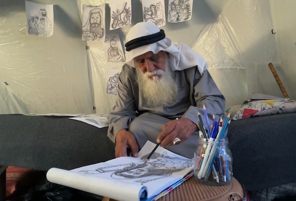 محمد زملط، رجل فلسطيني مسنّ اقتلعته الحرب من مخيم جباليا في شمال قطاع غزة، يحمل اليوم ريشته كوسيلة للبقاء، لا للفن فقط. في خيمته المتواضعة بمخيم البريج وسط القطاع، 12 أبريل/نيسان 2026، عدسة: يوسف أبو وطفة