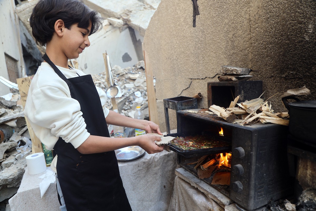 ياسر عياد، فتى فلسطيني يبلغ من العمر أربعة عشر عامًا، يمارس مهاراته في الطبخ على نار الحطب بجوار أنقاض منزل عائلته المدمر في مدينة غزة. غزة، 10 أبريل/نيسان 2026. تصوير: محمد الأسود