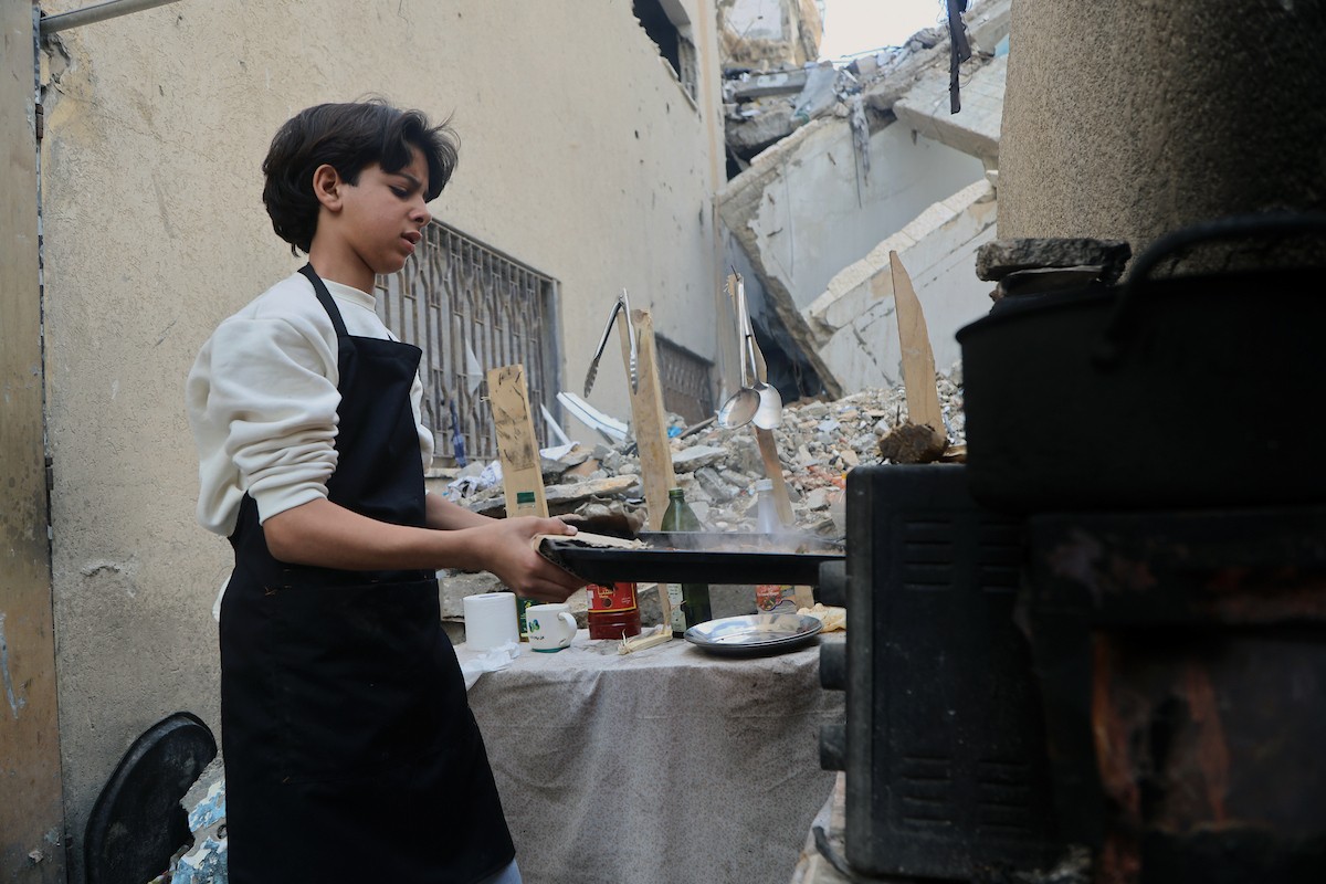 ياسر عياد، فتى فلسطيني يبلغ من العمر أربعة عشر عامًا، يمارس مهاراته في الطبخ على نار الحطب بجوار أنقاض منزل عائلته المدمر في مدينة غزة. غزة، 10 أبريل/نيسان 2026. تصوير: محمد الأسود