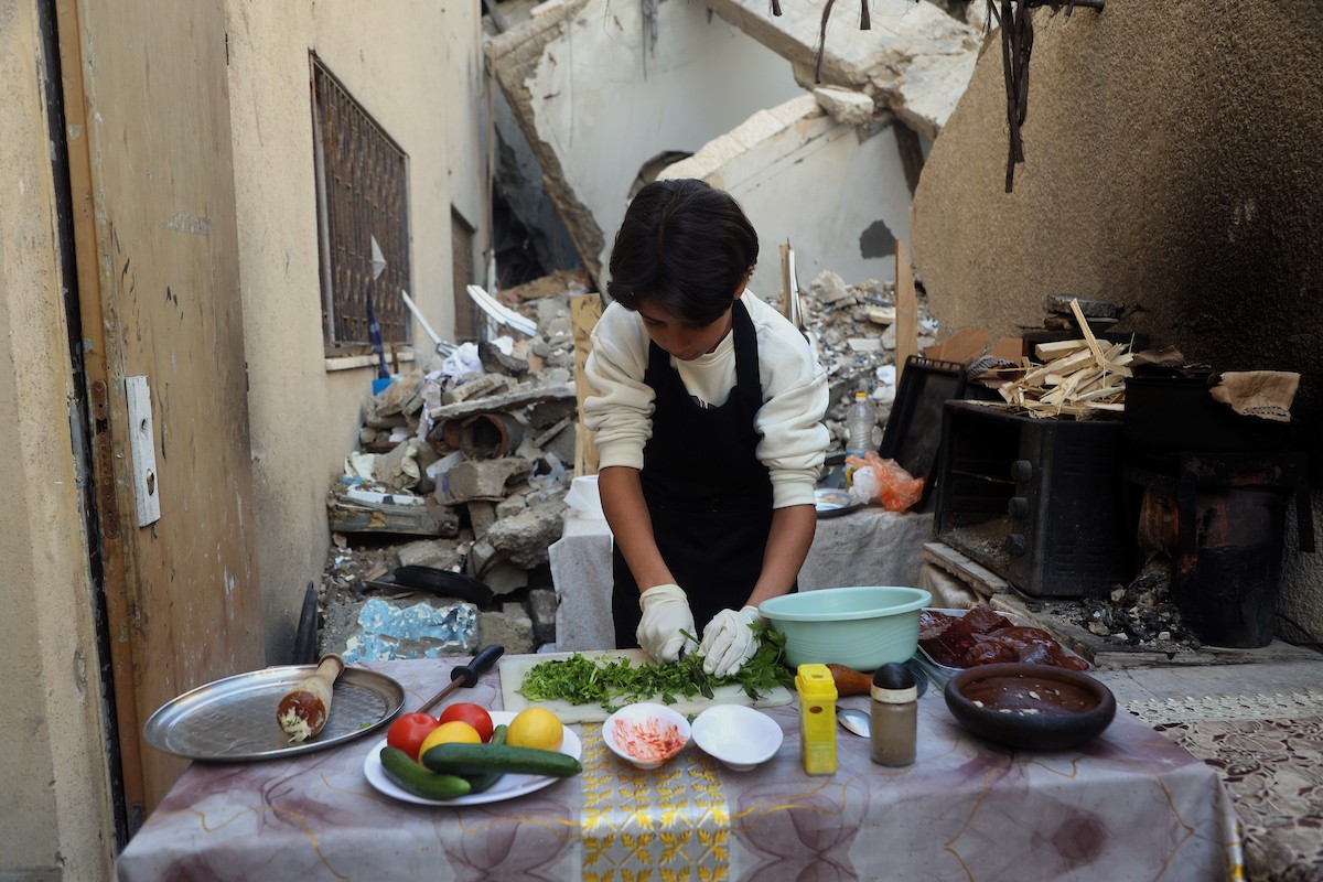 ياسر عياد، فتى فلسطيني يبلغ من العمر أربعة عشر عامًا، يمارس مهاراته في الطبخ على نار الحطب بجوار أنقاض منزل عائلته المدمر في مدينة غزة. غزة، 10 أبريل/نيسان 2026. تصوير: محمد الأسود