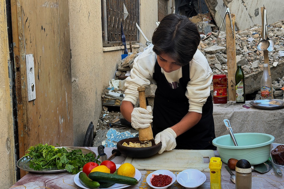 ياسر عياد، فتى فلسطيني يبلغ من العمر أربعة عشر عامًا، يمارس مهاراته في الطبخ على نار الحطب بجوار أنقاض منزل عائلته المدمر في مدينة غزة. غزة، 10 أبريل/نيسان 2026. تصوير: محمد الأسود