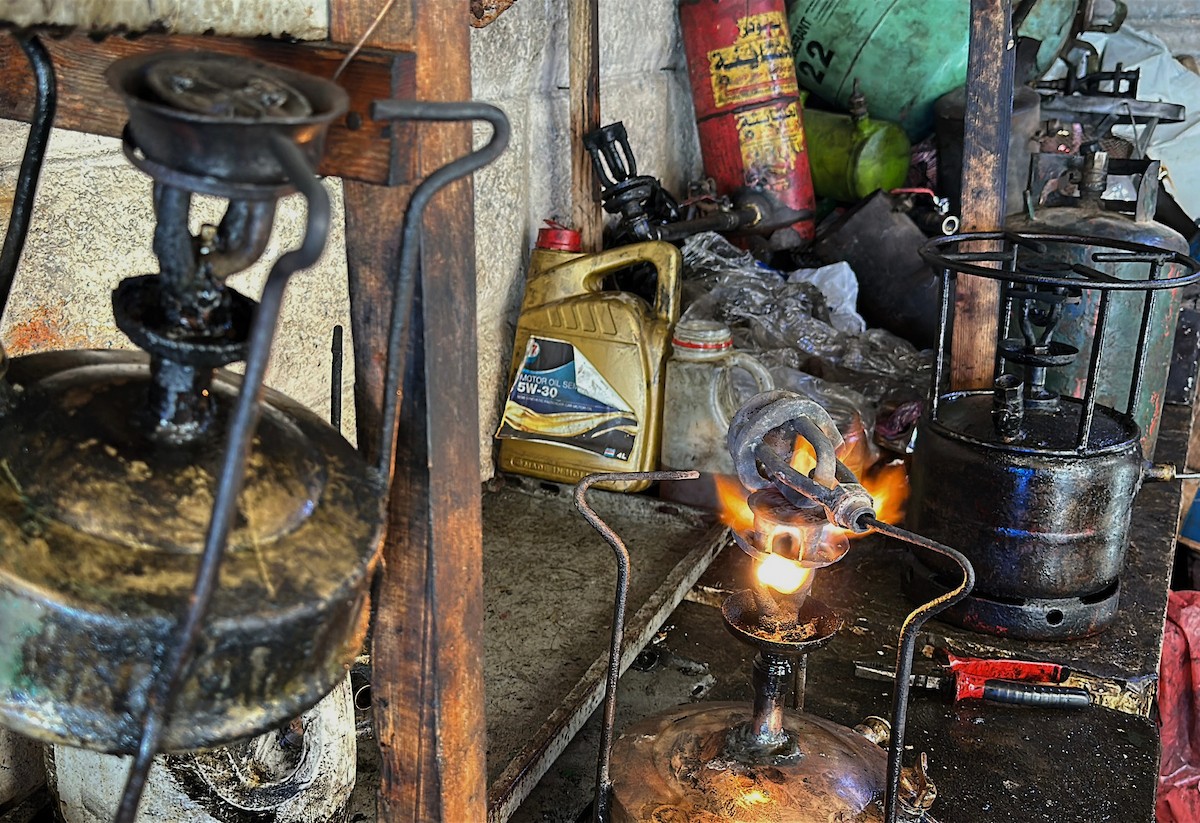 عادل عيسى، 63 عامًا، يُصلح مواقد الكيروسين القديمة في ورشته بمخيم الشاطئ، في مدينة غزة، صورة فوتوغرافية لهادي داود